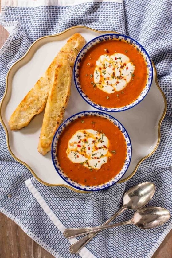Overhead vertical photo of a serving plate with two bowls of Roasted Red Pepper Soup next to Ridiculously Easy Focaccia Bread.