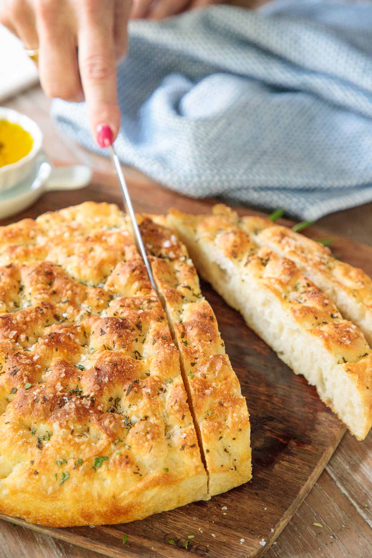 Vertical photo of a loaf of Ridiculously Easy Focaccia Bread being cut into slices.