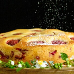 a Ridiculously Easy Fresh Strawberry Cake on a wood platter decorated with spring flowers.
