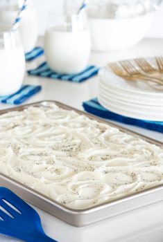 Vertical picture of Lemon Poppy Seed Sheet Cake with glasses of milk and a stack of white plates