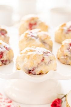 Vertical closeup photo of a batch of Ridiculously Easy Lemon Raspberry Scones on a white pedestal stand.