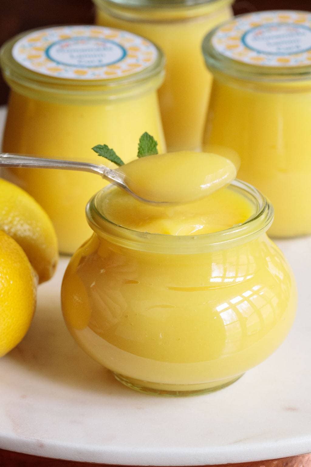 Photo of glass jars filled with Ridiculously Easy Microwave Lemon Curd and a spoonful of lemon curd over the center jar.