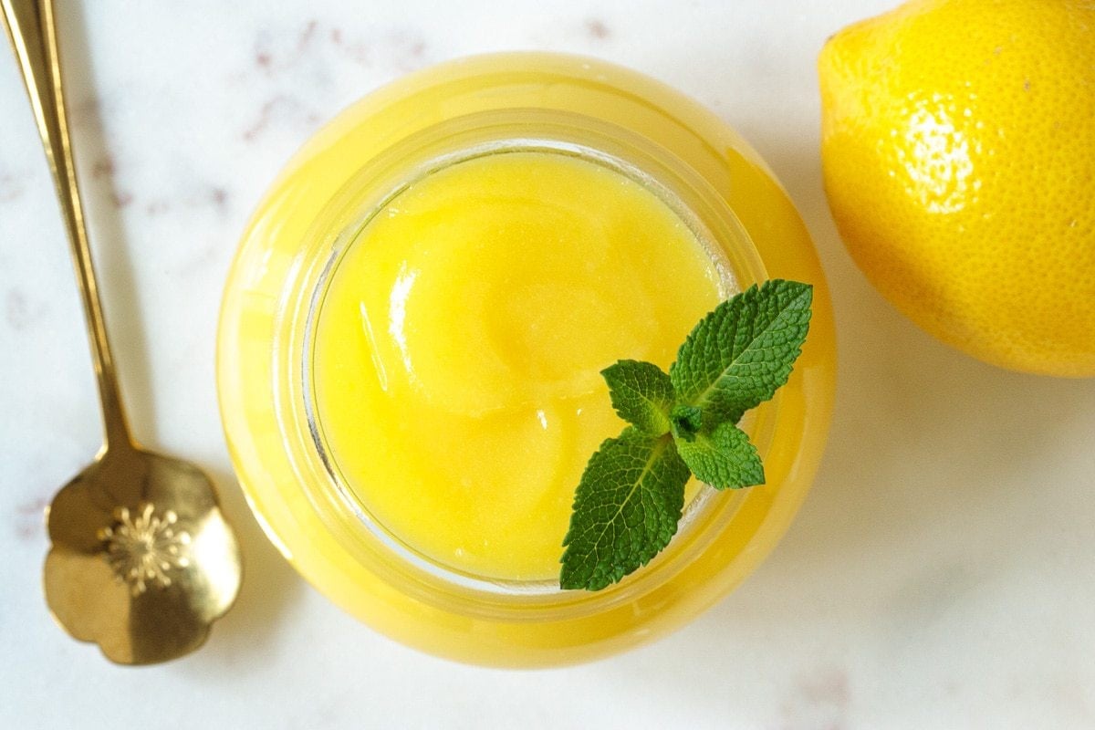 Overhead closeup photo of a glass canning jar of Ridiculously Easy Microwave Lemon Curd on a quartz countertop.