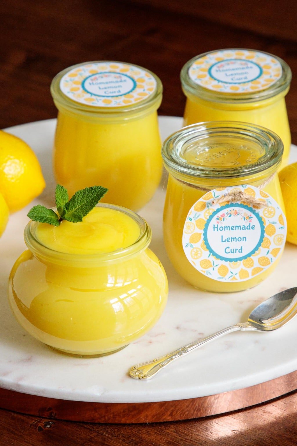 Vertical photo of Weck glass jars of Ridiculously Easy Microwave Lemon Curd on a round marble surface.