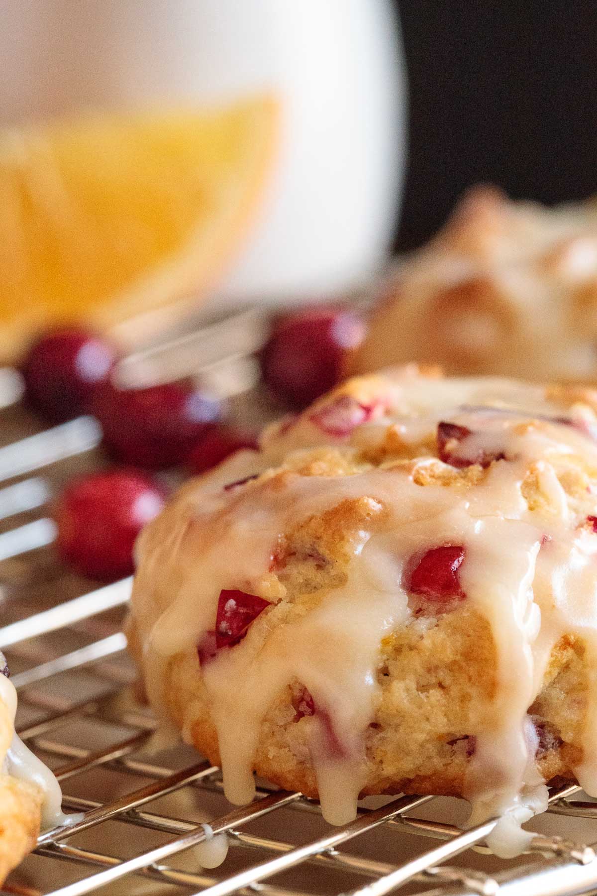 Vertical extreme closeup photo of a batch of Ridiculously Easy Orange Cranberry Scones on a metal cooling rack with fresh cranberries and orange slices in the background.