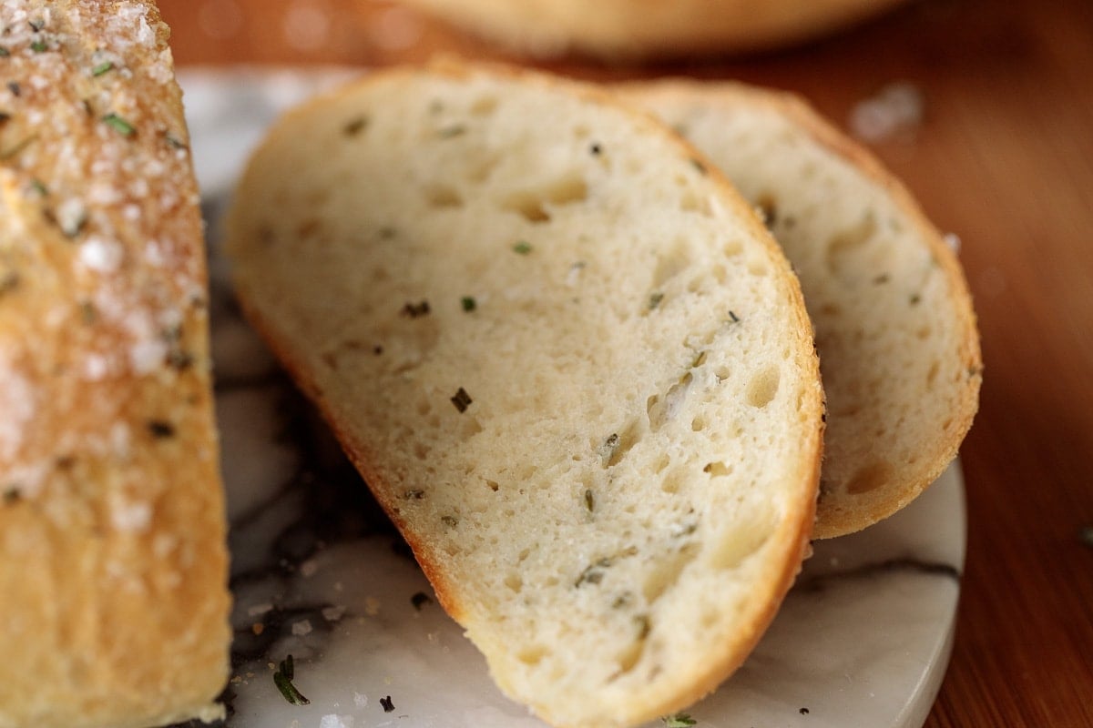 Horizontal extreme closeup of slices of Ridiculously Easy Rosemary Bread on a marble platter.