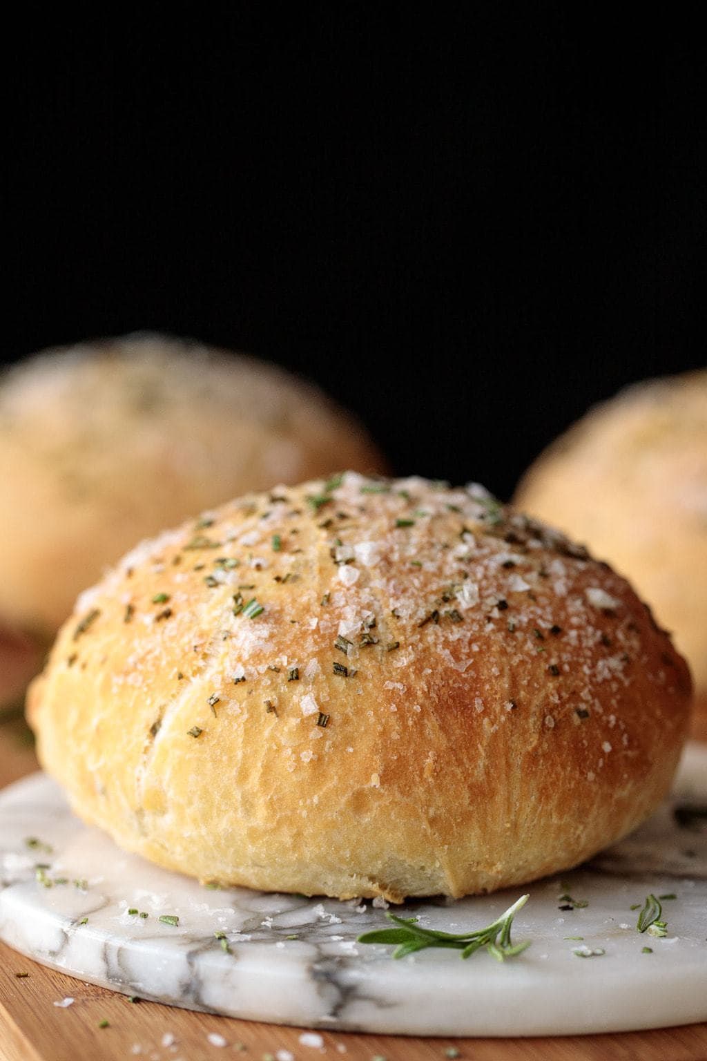 Extreme closeup vertical photo of a loaf of Ridiculously Easy Rosemary Bread on a white marble platter.