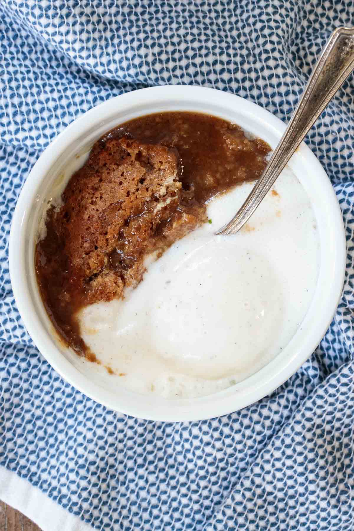 Closeup photo of an individual serving bowl of Ridiculously Easy Sticky Toffee Pudding with a scoop of vanilla bean ice cream.