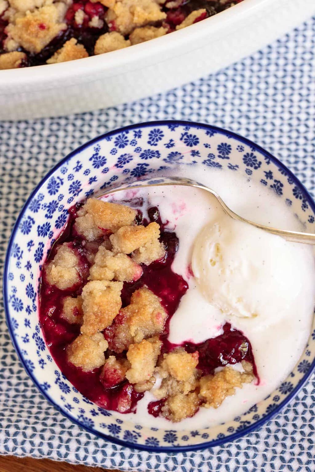 Overhead vertical closeup photo of an individual serving of Ridiculously Easy Summer Berry Crisp in a blue and white patterned serving bowl.