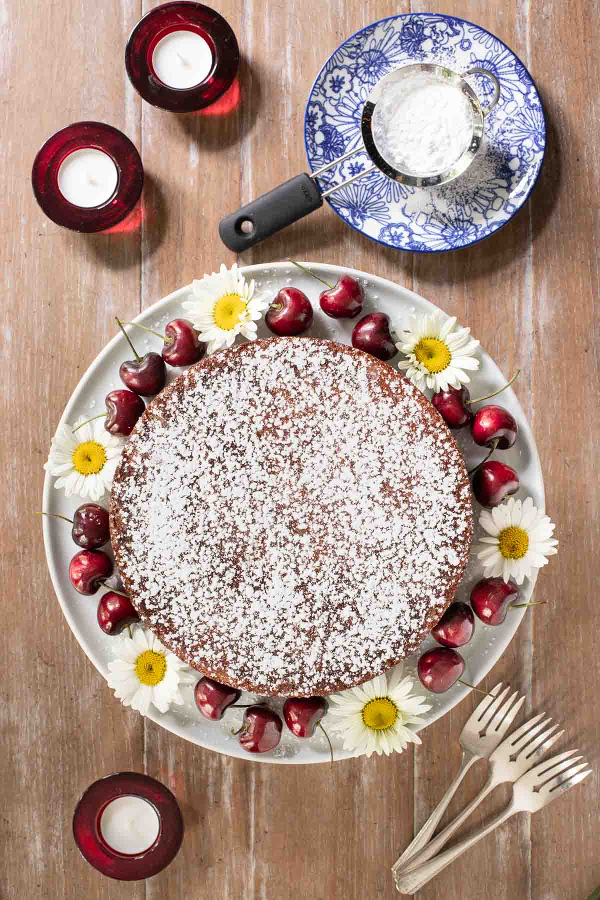 Overhead vertical photo of Ridiculously Fresh Sweet Cherry Almond Cake garnished with fresh cherries and wild flowers on a wood table.