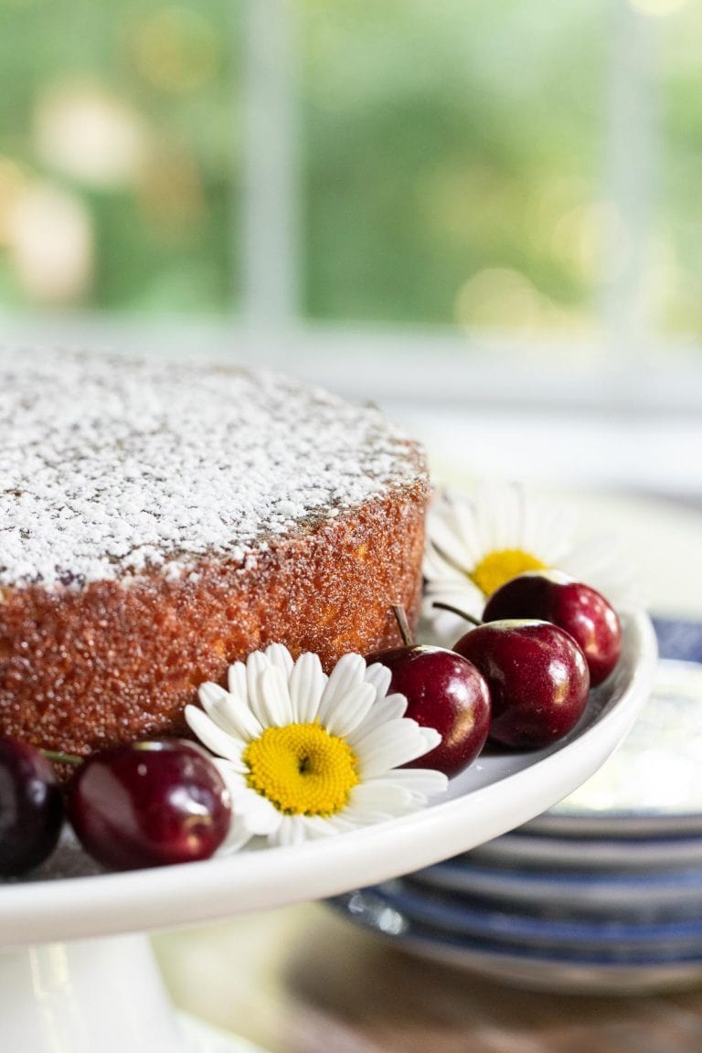Vertical close up picture of cherry almond cake on a white cake stand