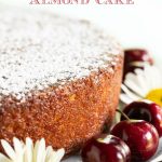 Closeup vertical photo of the glazed side of a Ridiculously Fresh Sweet Cherry Almond Cake decorated with daisies and fresh, ripe cherries.