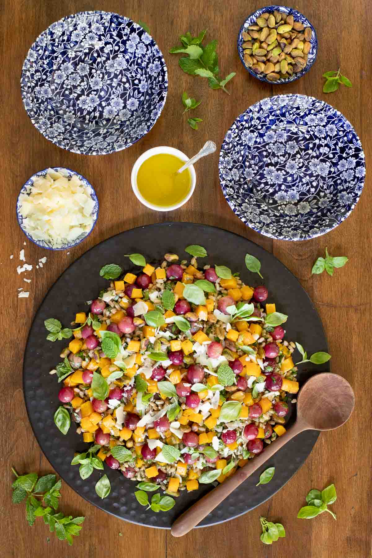 Overhead vertical photo of Roasted Butternut Farro Salad in a black charger on a wooden table.