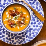 Overhead vertical closeup photo of Roasted Butternut Squash Soup with crispy pancetta on a blue and white plate