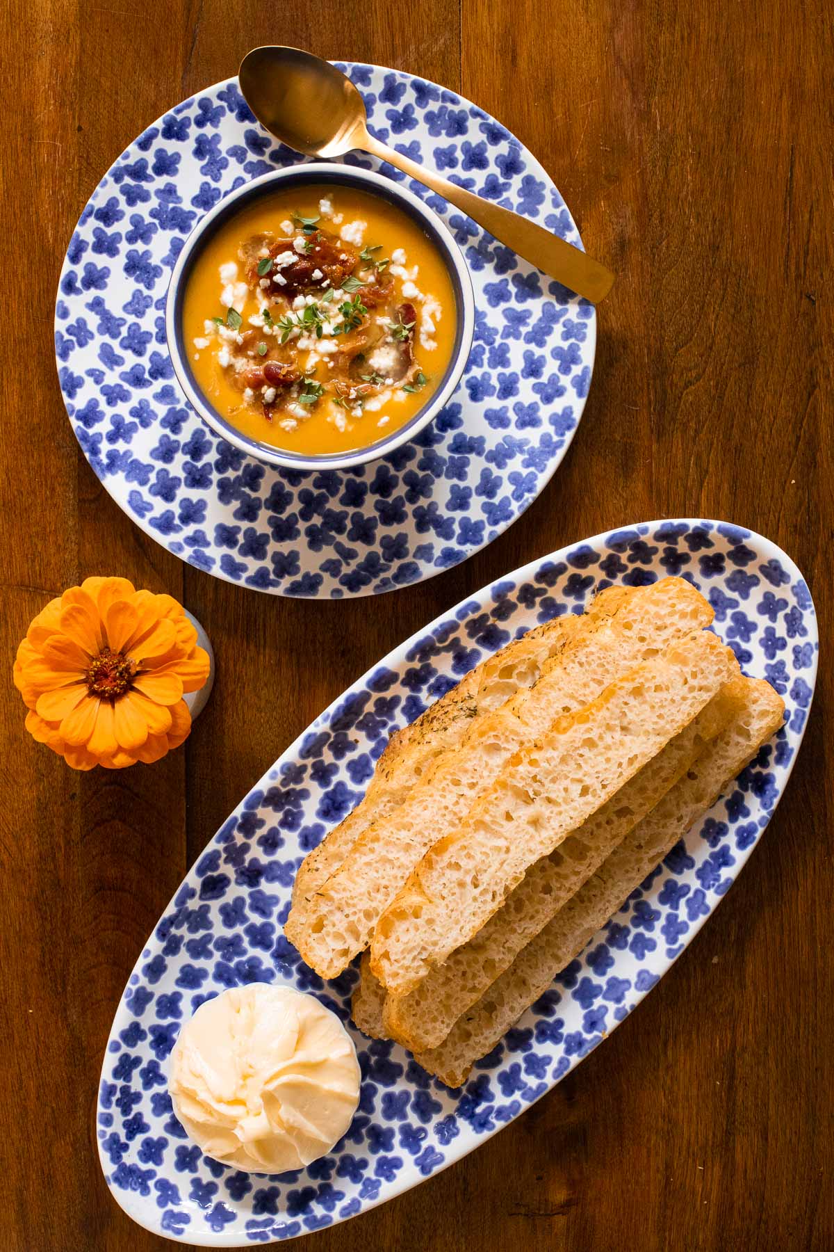 Overhead vertical photo of a bowl of Roasted Butternut Squash Soup with Crispy Pancetta with an oblong plate of homemade focaccia bread.