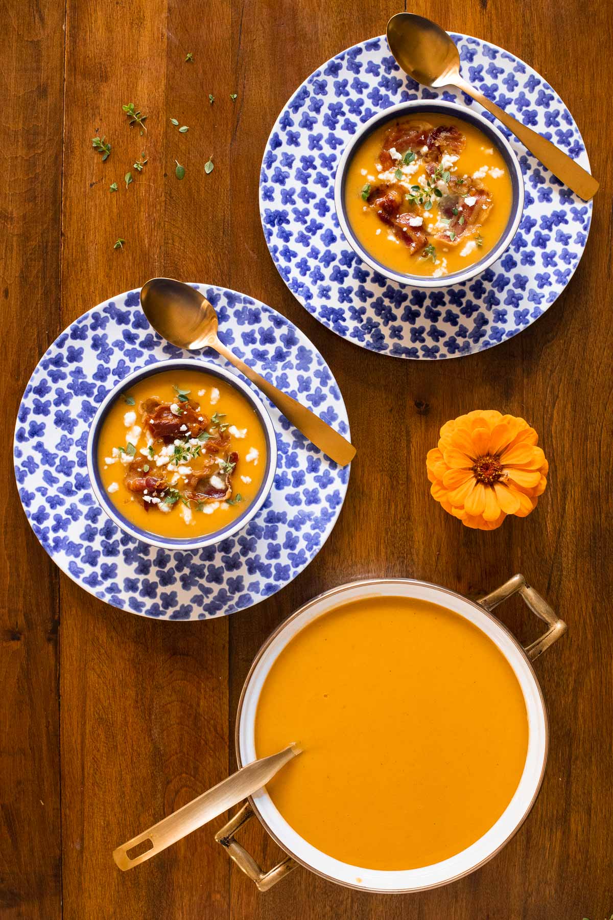 Overhead vertical photo of a pot and serving bowls of Roasted Butternut Squash Soup with Crispy Pancetta on a wood table.