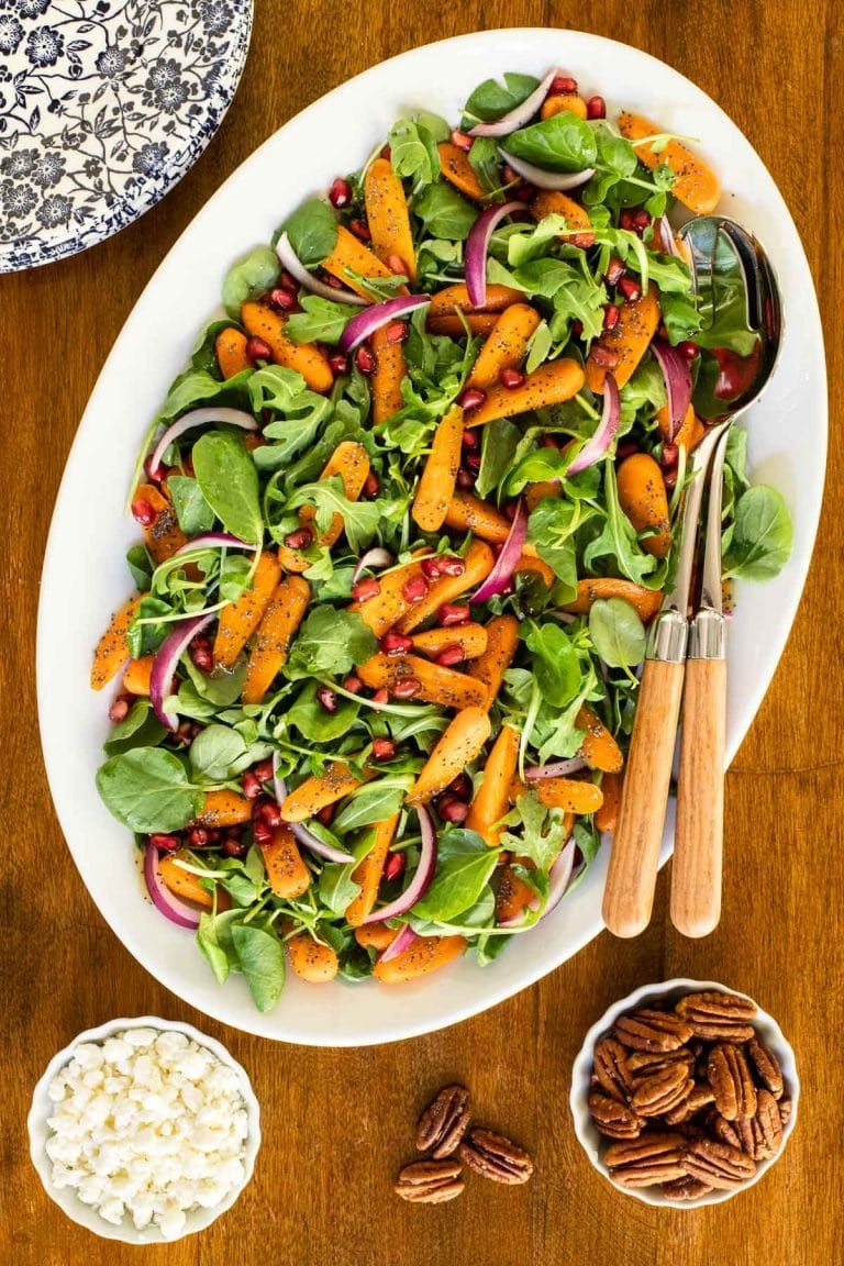 Vertical overhead picture of Roasted Carrot Salad on a white oval platter with salad tongs and toppings.