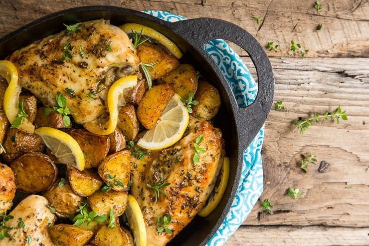 Overhead photo of a cast iron oval baking pan of Lemon Garlic Roasted Chicken and Potatoes on a barnyard table.