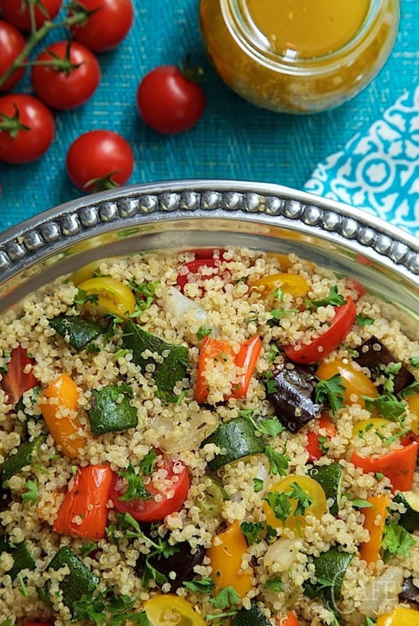 Closeup overhead photo of Roasted Ratatouille Quinoa Salad on a silver platter with a vine of red cherry tomatoes and a jar of dressing beside it.