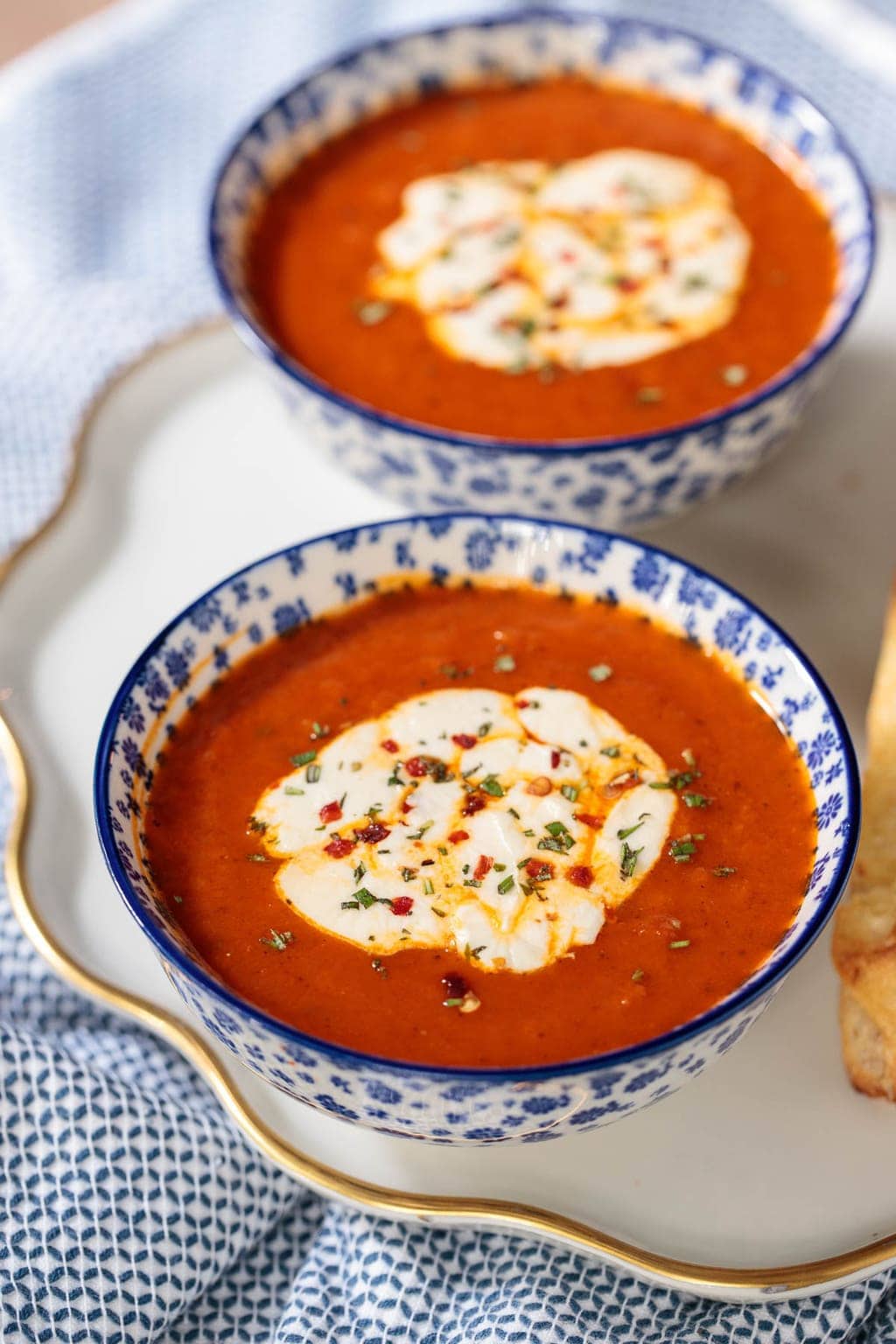 Vertical photo of Roasted Red Pepper Tomato Soup topped with melted mozzarella cheese in blue and white patterned bowls.
