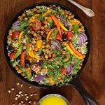 Overhead picture of roasted veggie salad in a cast iron skillet on a wooden table with dressing