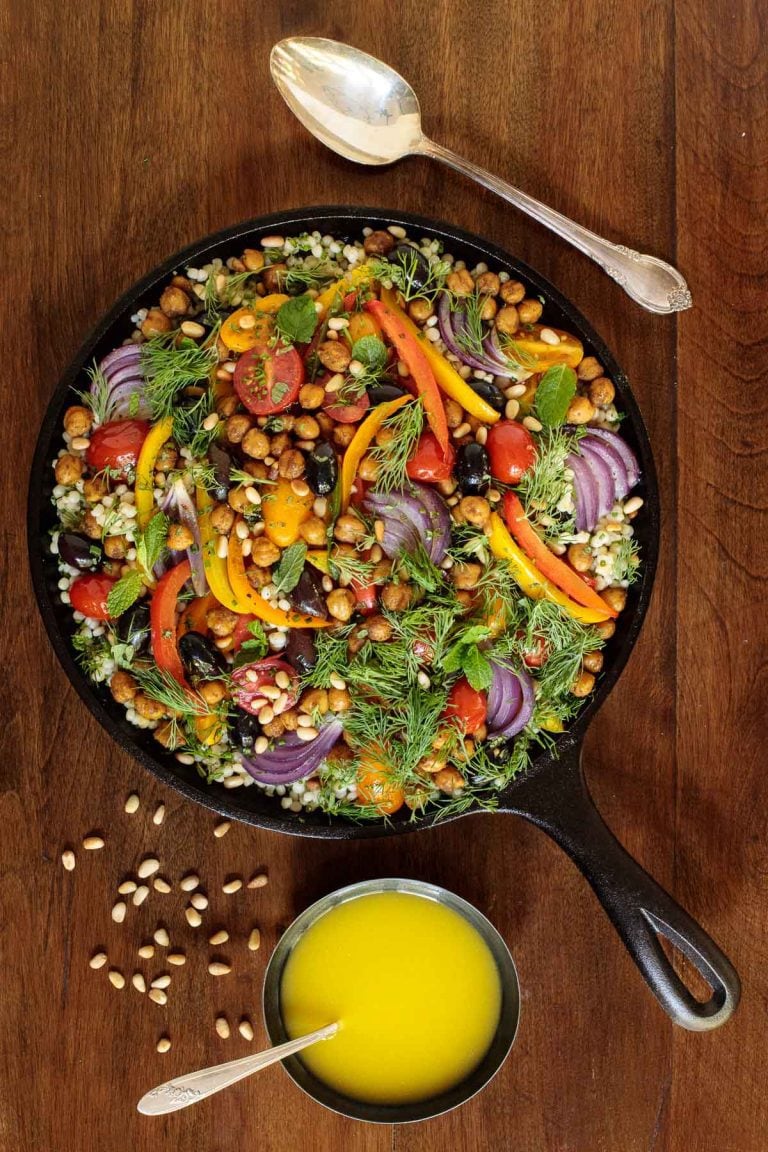 Roasted veggie salad in a cast iron skillet on a wooden table with dressing
