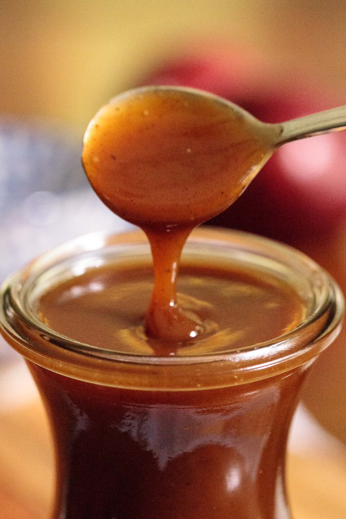 Ultra closeup photo of a spoon of Apple Cider Caramel Sauce being drizzled back into a glass jar of the sauce.