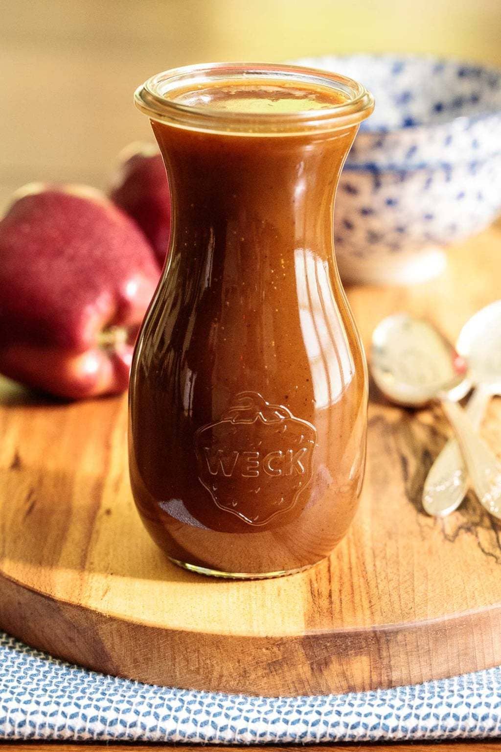 A photo of a glass Weck jar filled with Apple Cider Caramel Sauce on a wood presentation platter.