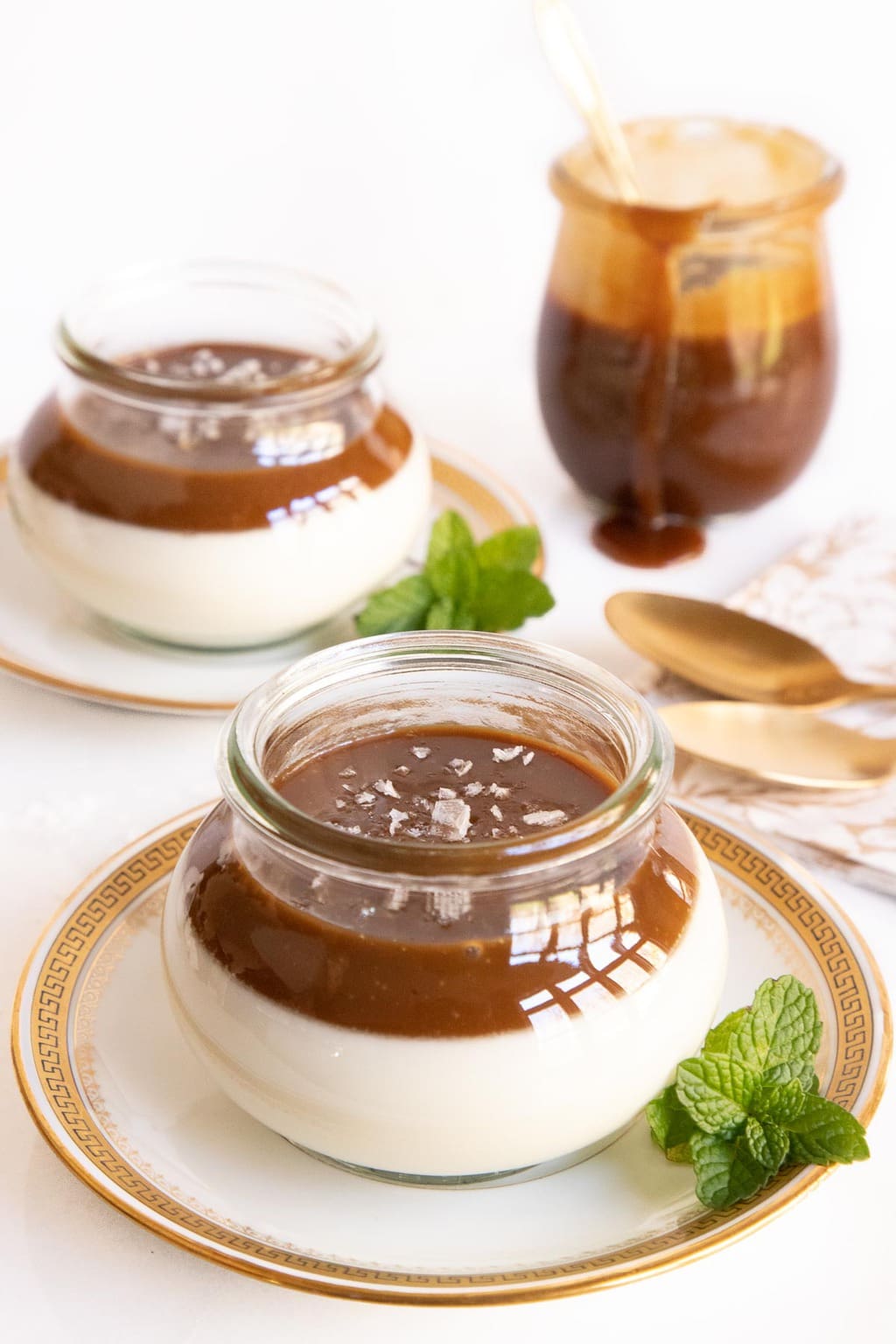 Vertical photo of glass Weck jars filled with Salted Butterscotch Panna Cotta on gold rimmed serving plates.