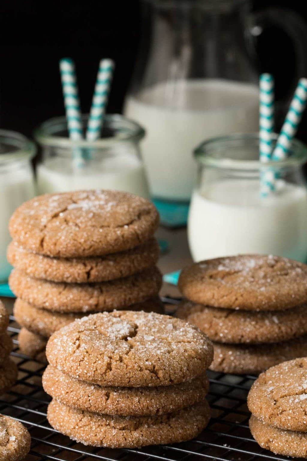 Vertical photo of Sea Salted Brown Sugar Cookies stacked on a cooling rack with glasses and a pitcher of milk in the background.