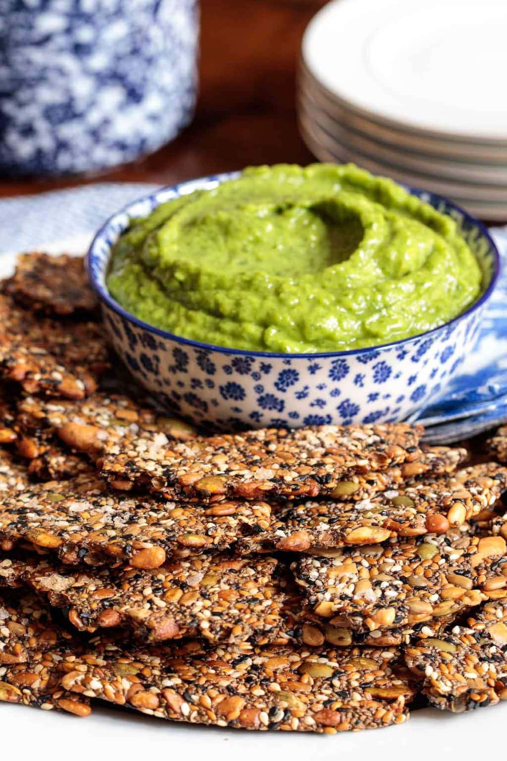 Vertical photo of Pine Nut Seeded Crackers with a dish of avocado dip.