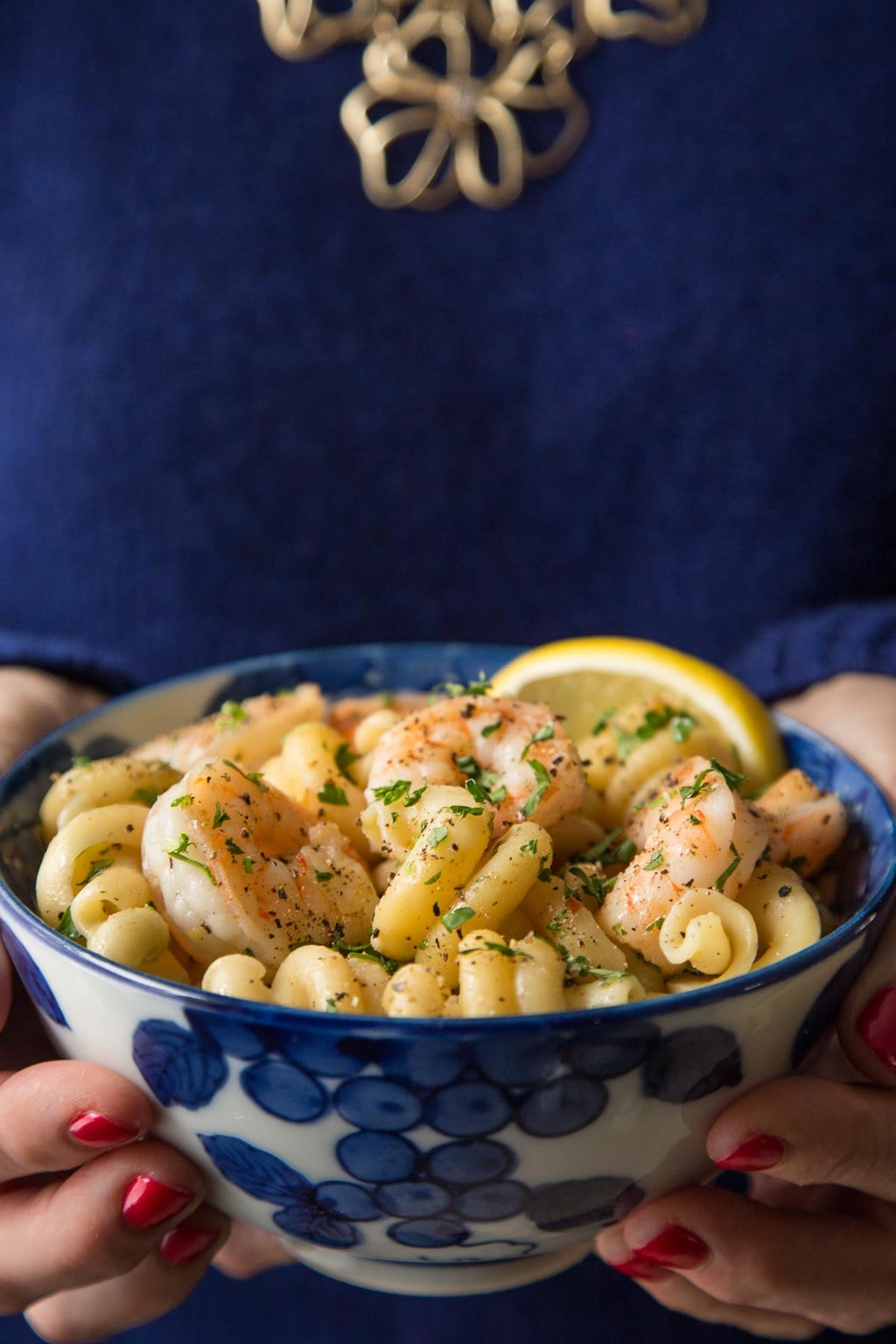 Photo of a woman holding a blue and white patterned bowl of Skillet Pasta Shrimp Scampi.