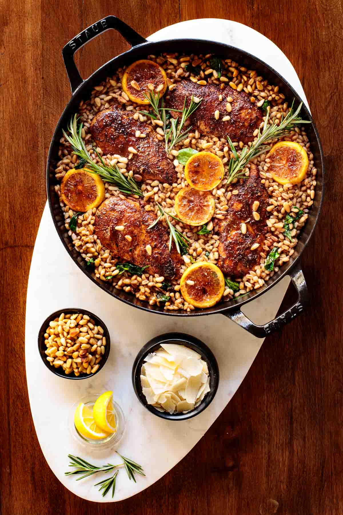 Overhead photo of Skillet Lemon Rosemary Chicken and Farro in a cast iron braised pan on white marble.