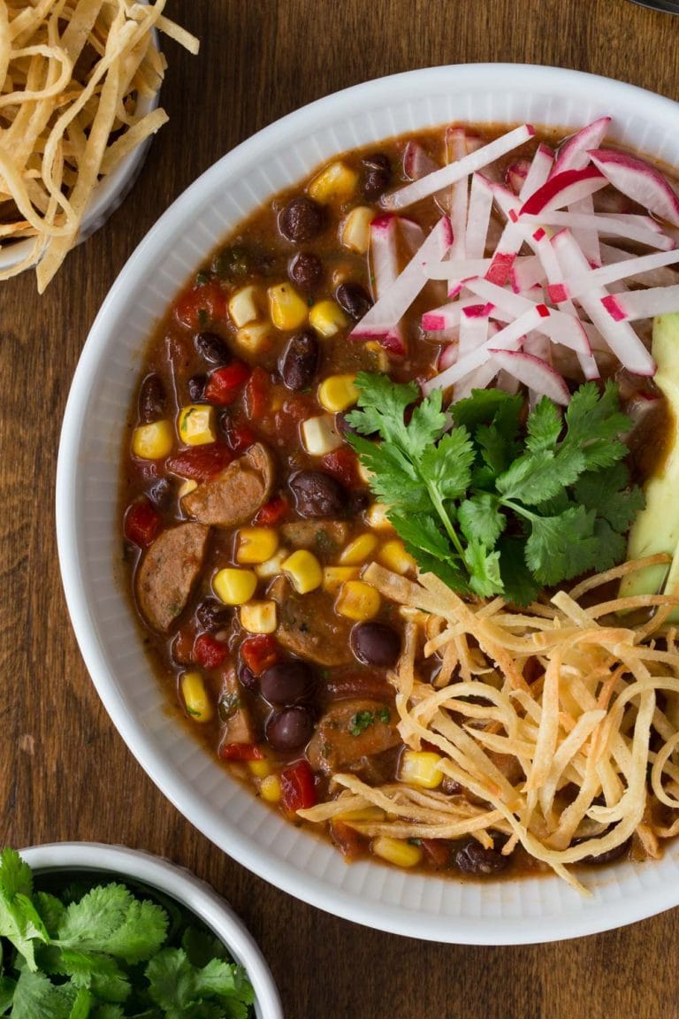 Vertical overhead picture of slow cooker black bean and chicken sausage tortilla soup with toppings