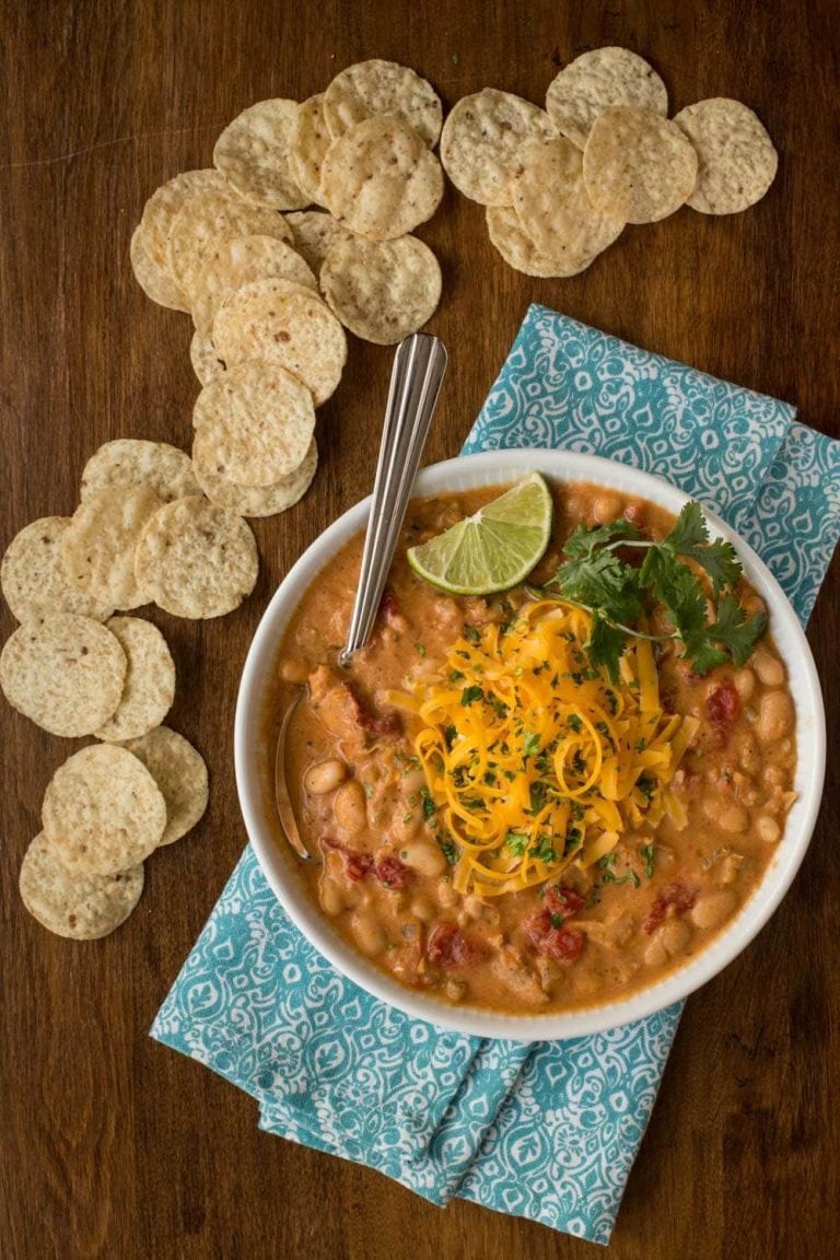 Overhead picture of buffalo chicken chili in a white bowl with chips and a blue napkin