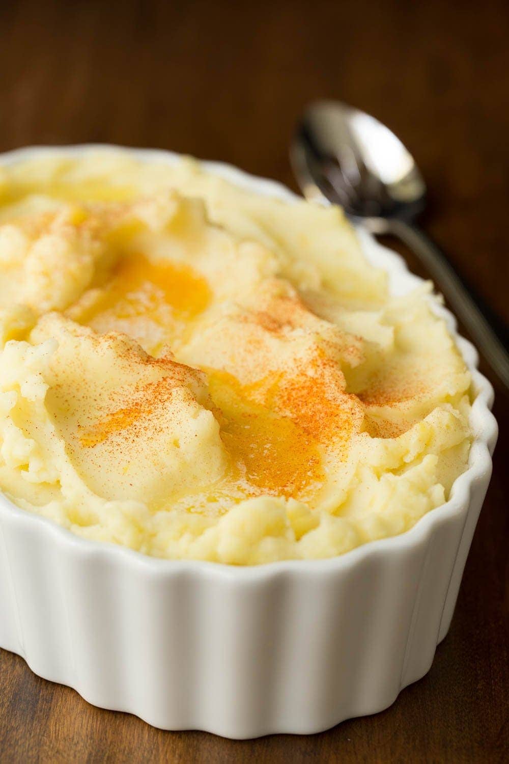 Vertical closeup photo of Slow Cooker Buttermilk Mashed Potatoes in a white scalloped serving dish.