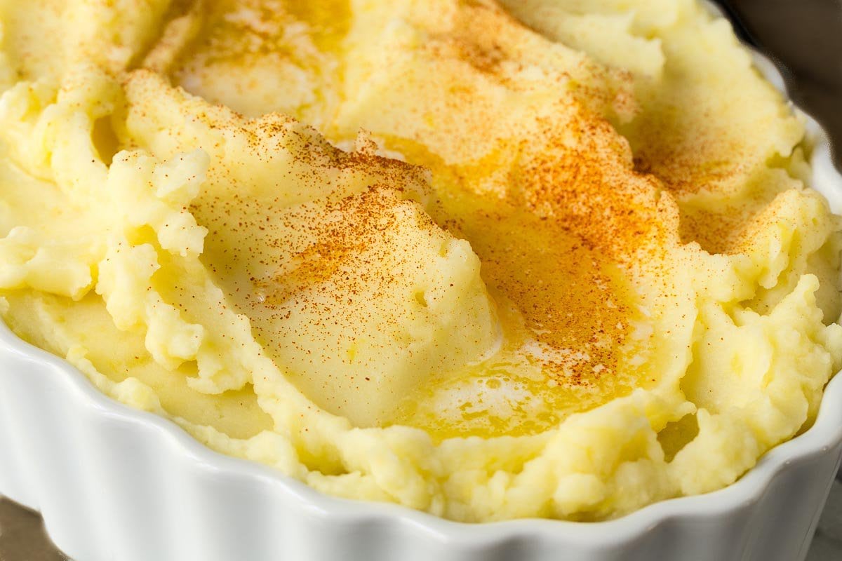 Closeup photo of a dish of Slow Cooker Buttermilk Mashed Potatoes with melted butter on top.