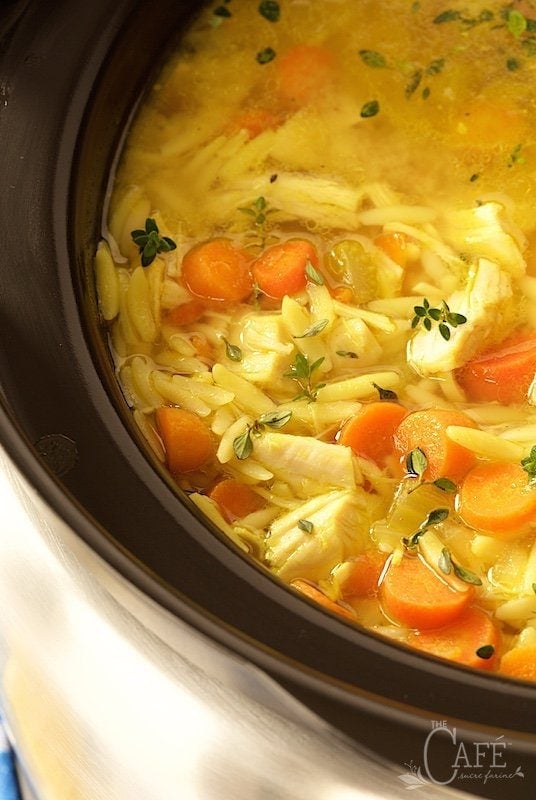 Close up vertical photo of Slow Cooker Lemon Orzo Chicken Soup in a slow cooker pot.