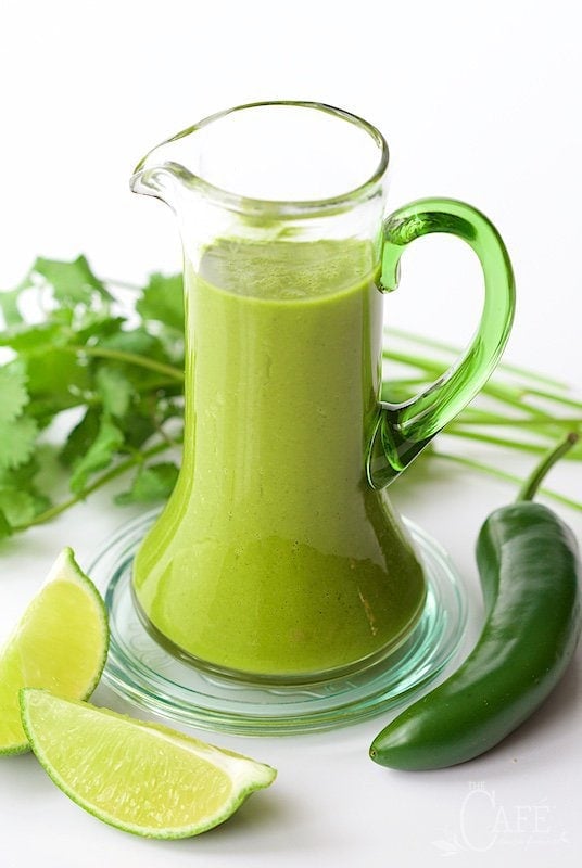 Vertical picture of spicy cilantro dressing in a glass pitcher garnished with fresh cilantro, jalapeno, and lime
