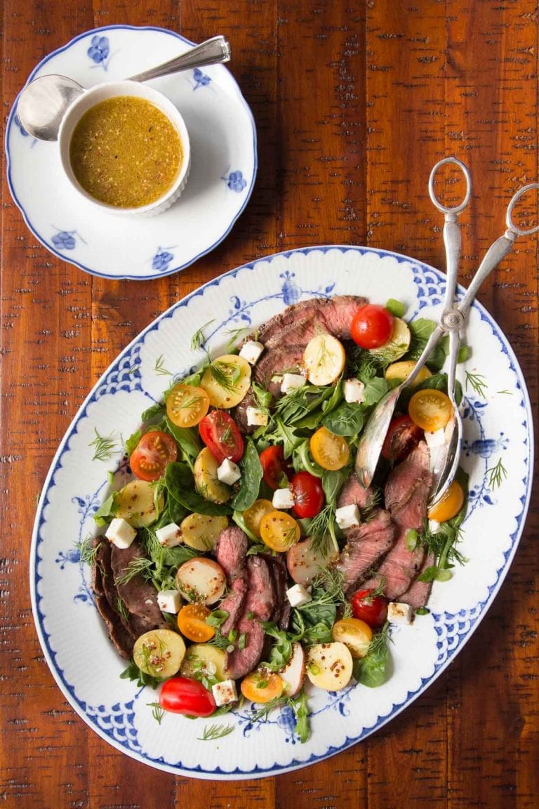 Steak and potato salad on a blue and white platter with dressing on a wooden table