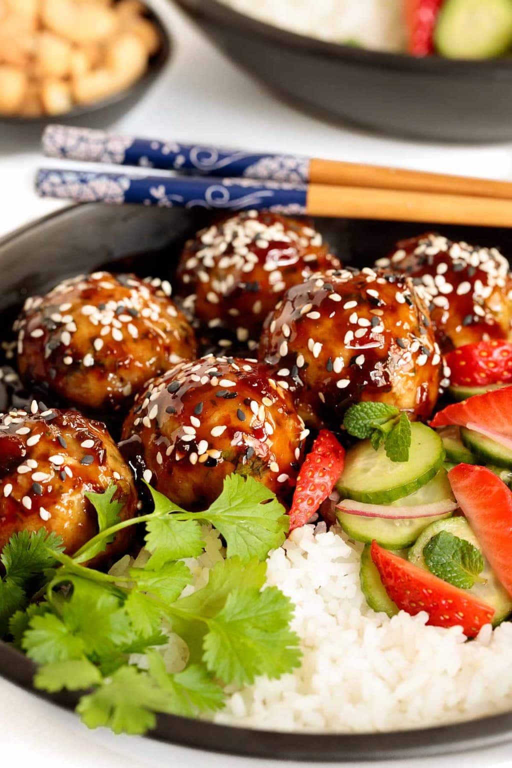 Close up vertical photo of Strawberry Balsamic Chicken Meatball Rice Bowls in a black individual serving bowl garnished with cilantro and sesame seeds.