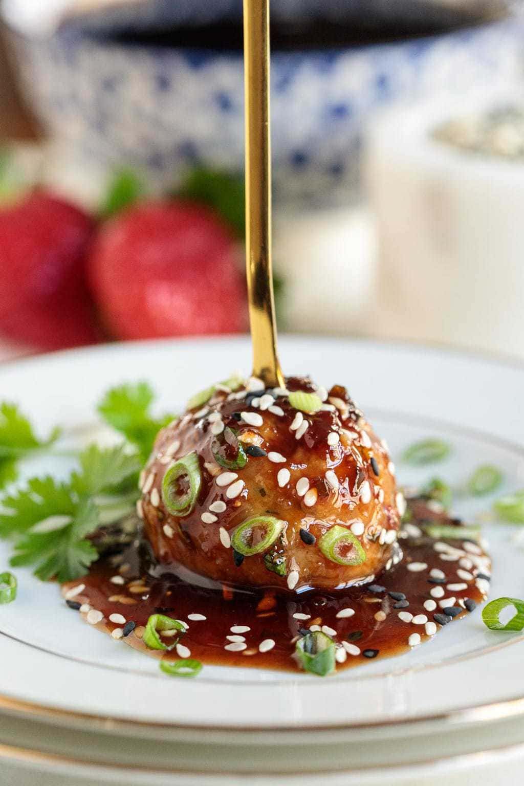 Vertical closeup photo of a Strawberry Balsamic Glazed Chicken Meatball with a gold appetizer fork stuck in the top.