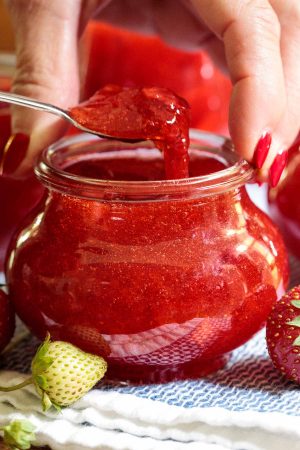 Close up photo of a person scooping Easy Strawberry Freezer Jam out of a Weck canning jar.