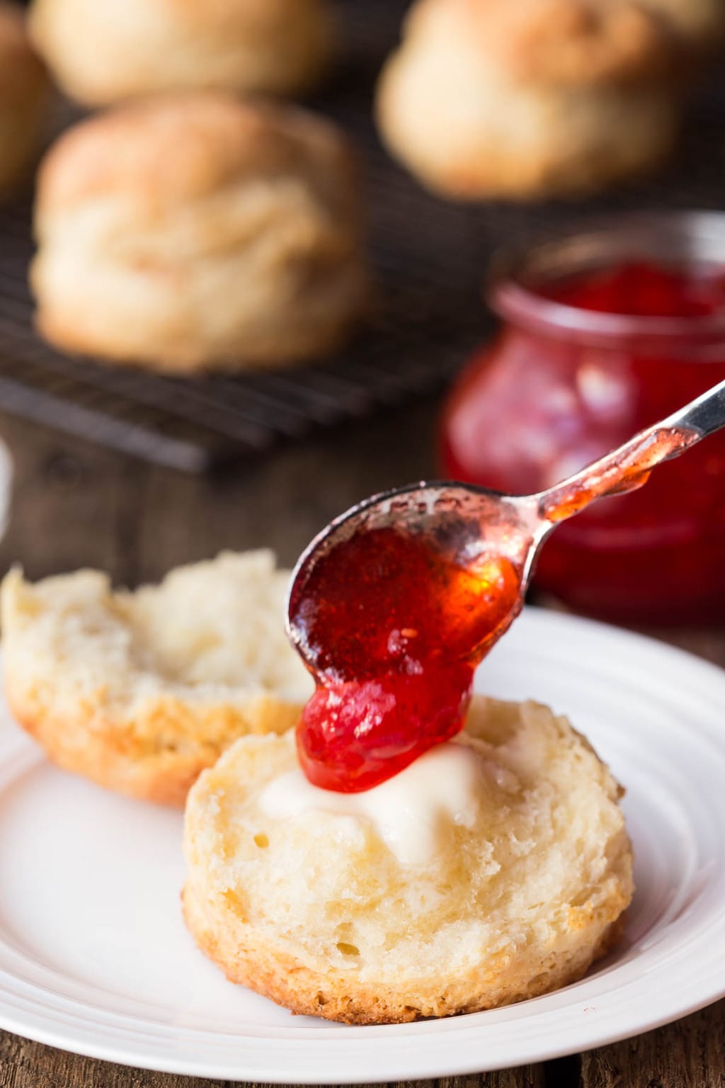 Vertical photo of Strawberry Freezer Jam being spooned over a Ridiculously Easy Biscuit on a white serving plate.