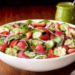 Horizontal closeup photo of a Strawberry Spinach Salad in a white serving bowl on a wood table.