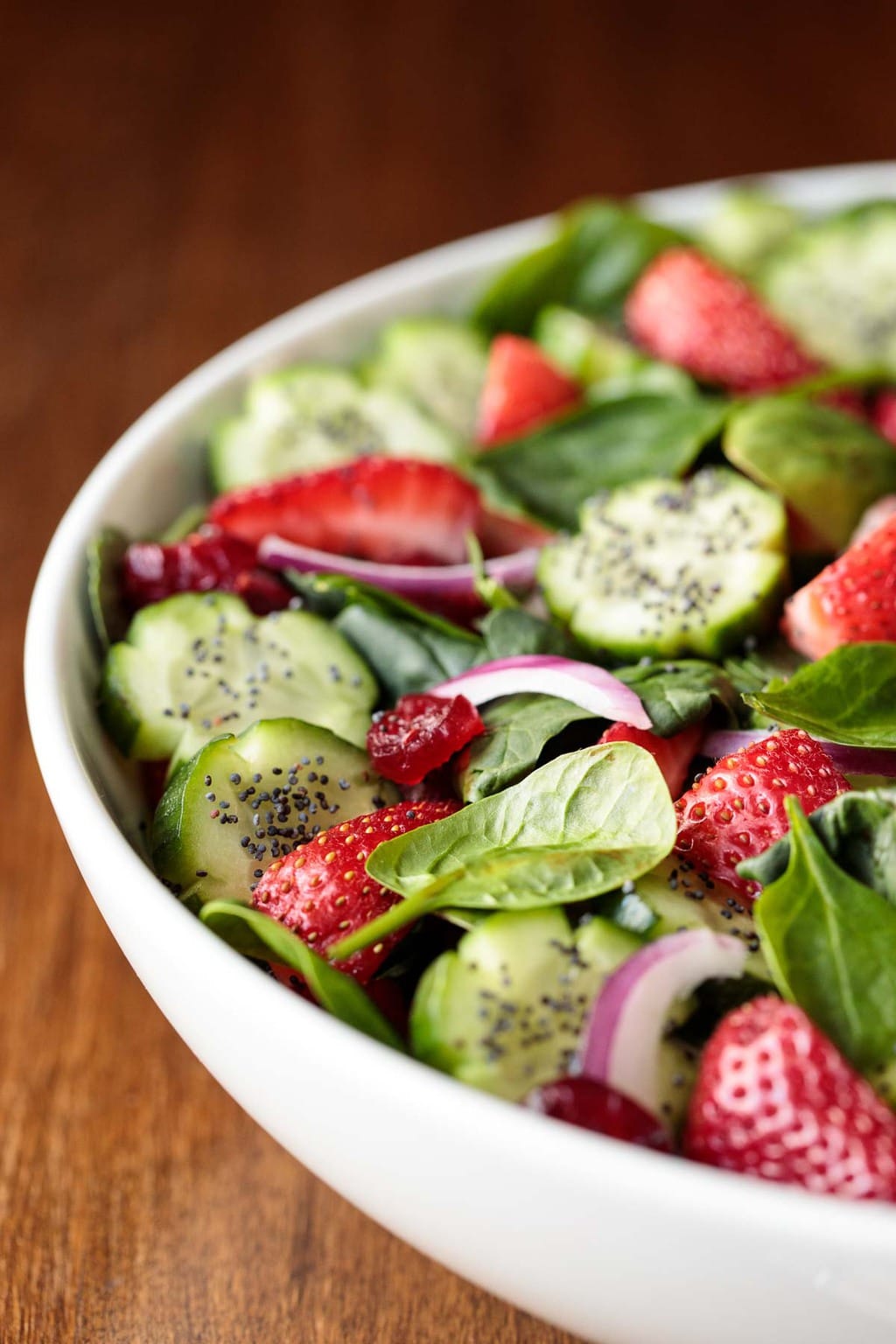 Vertical closeup photo of a Strawberry Spinach Salad in a white serving bowl on a wood table.