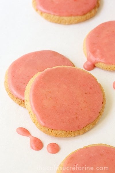 Overhead photo of Strawberry Glazed Butter Thin cookies on a white cutting board.