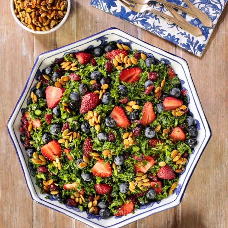 Overhead picture of summer kale salad on a wooden table with a blue and white napkin