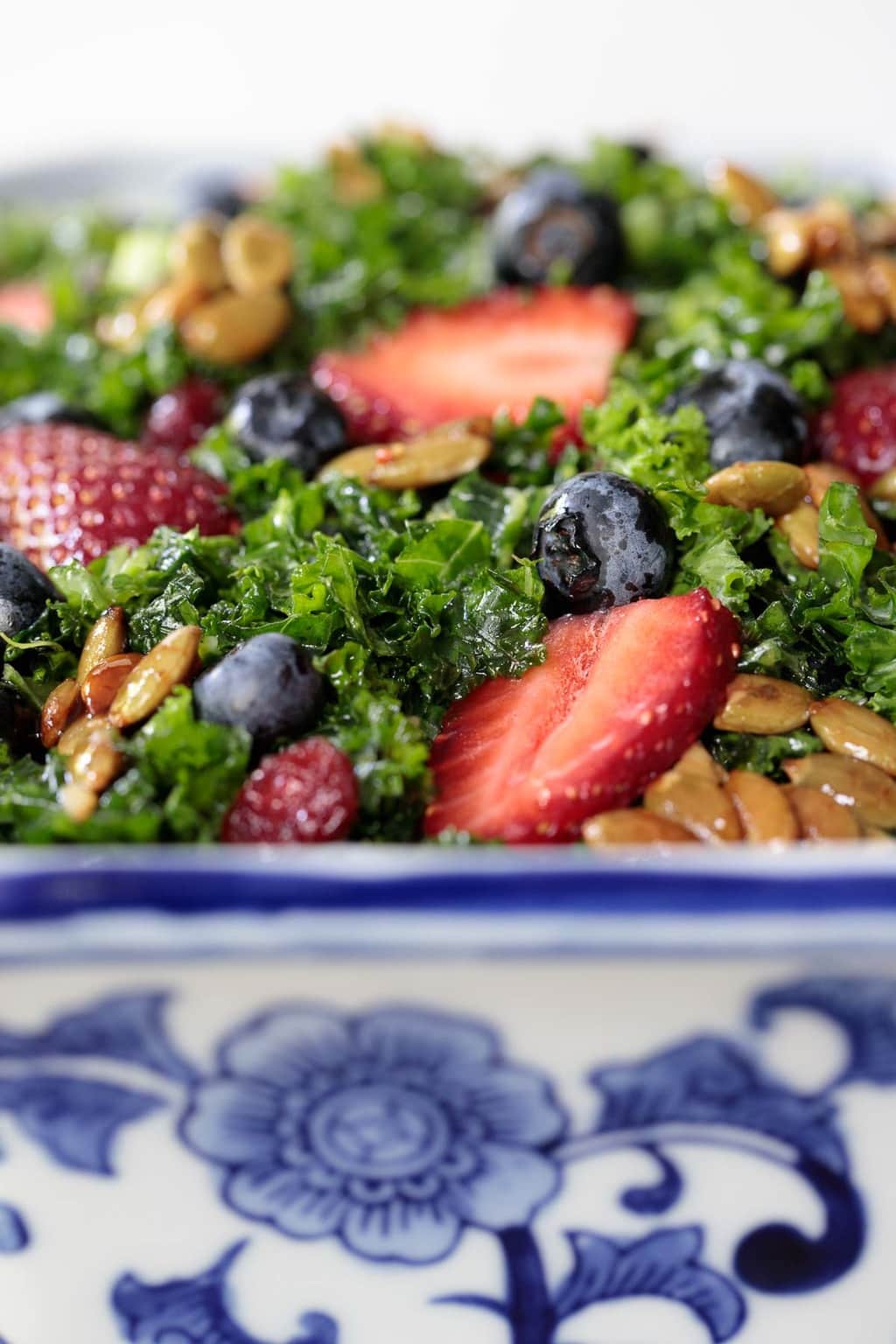 Side Closeup photo of a blue and white serving bowl filled with Strawberry Kale Salad with Honey Lemon Dressing.