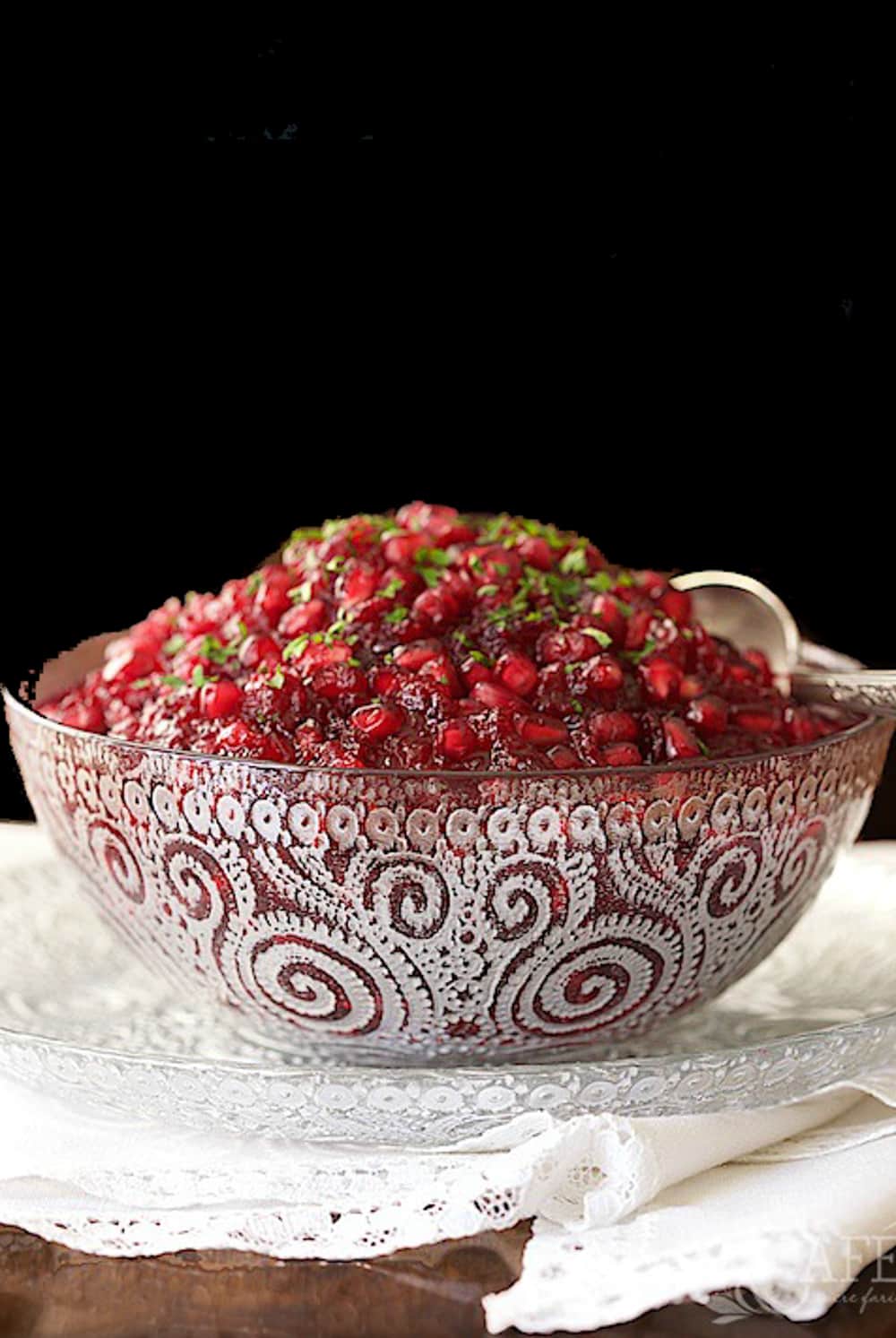 Side photo of a etched glass serving dish filled with Easy Cranberry Pomegranate Sauce.